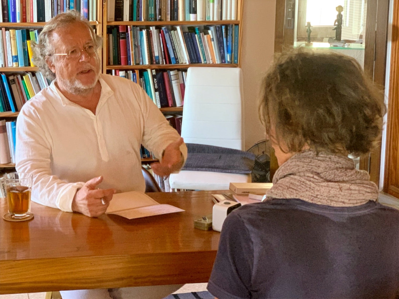 Ärztliches Gespräch am Tisch, im Hintergrund ein Bücherregal