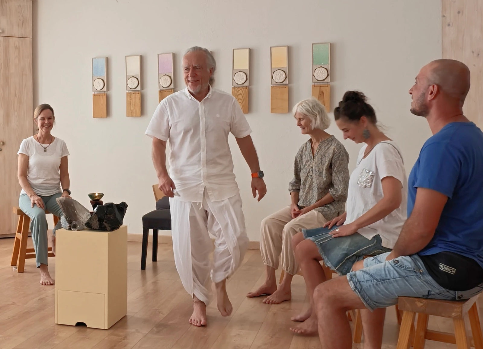 Dr. Hemmerich steht in der Mitte einer Gruppe, die im hellen Übungsraum auf Hockern sitzt