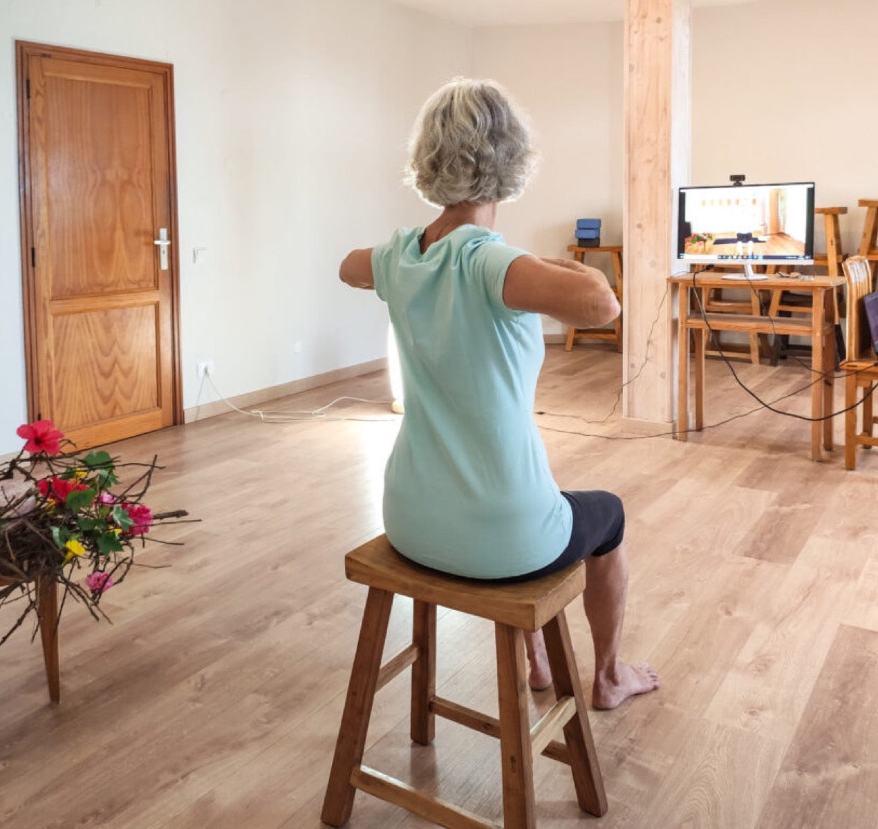 Eine Frau übt im Sitzen auf einem Hocker, die Arme zur Seite gestreckt