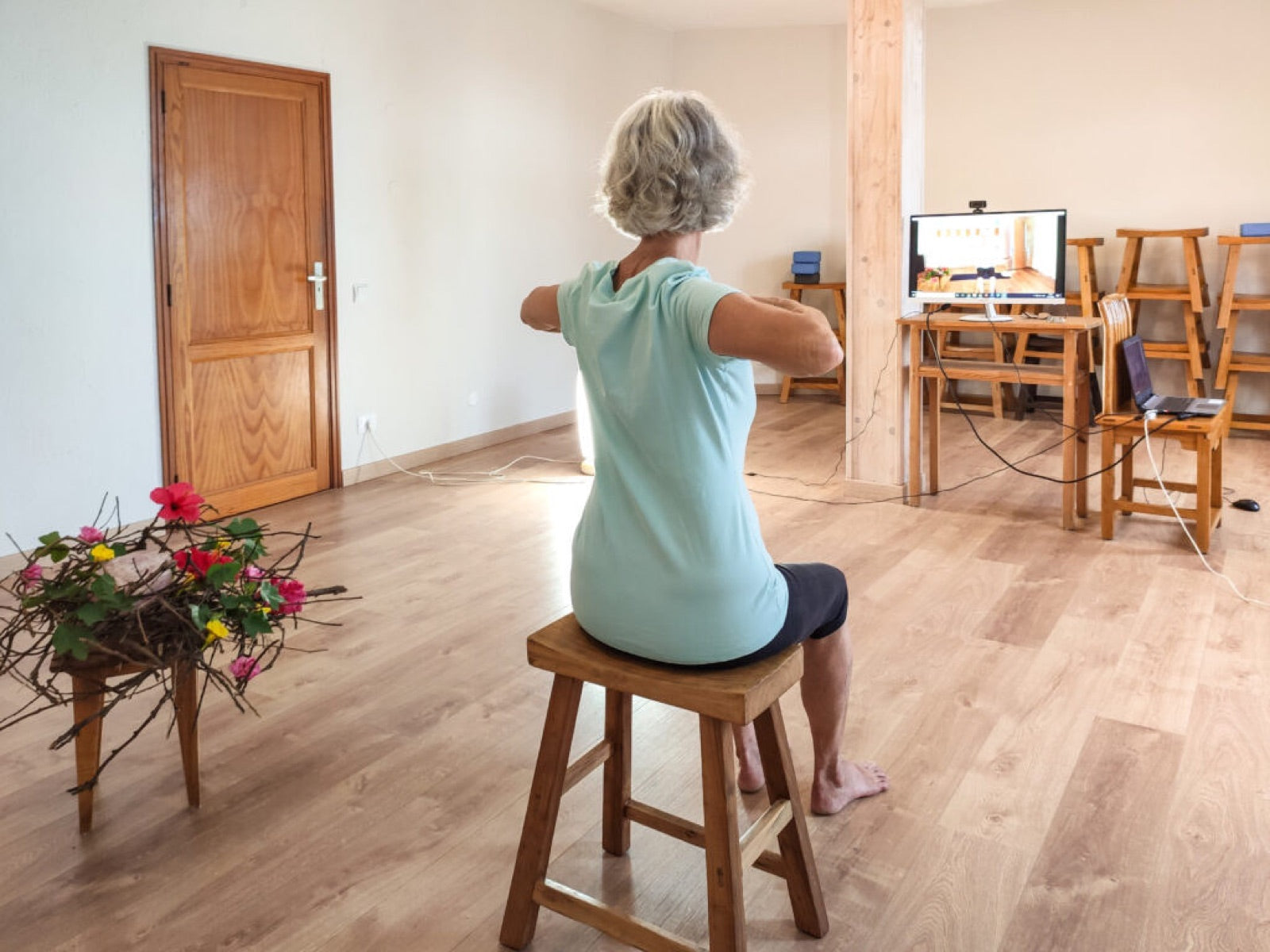 Eine Frau übt im Sitzen auf einem Hocker, die Arme zur Seite gestreckt
